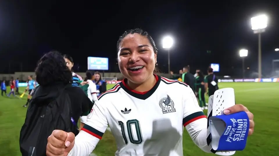 Citlalli Reyes smiles on the pitch holding her shin guards after a Mexico match